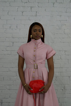 Woman in a pink dress holding a red bag against a white brick wall