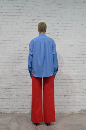 Person wearing a blue shirt and red pants standing against a white brick wall.