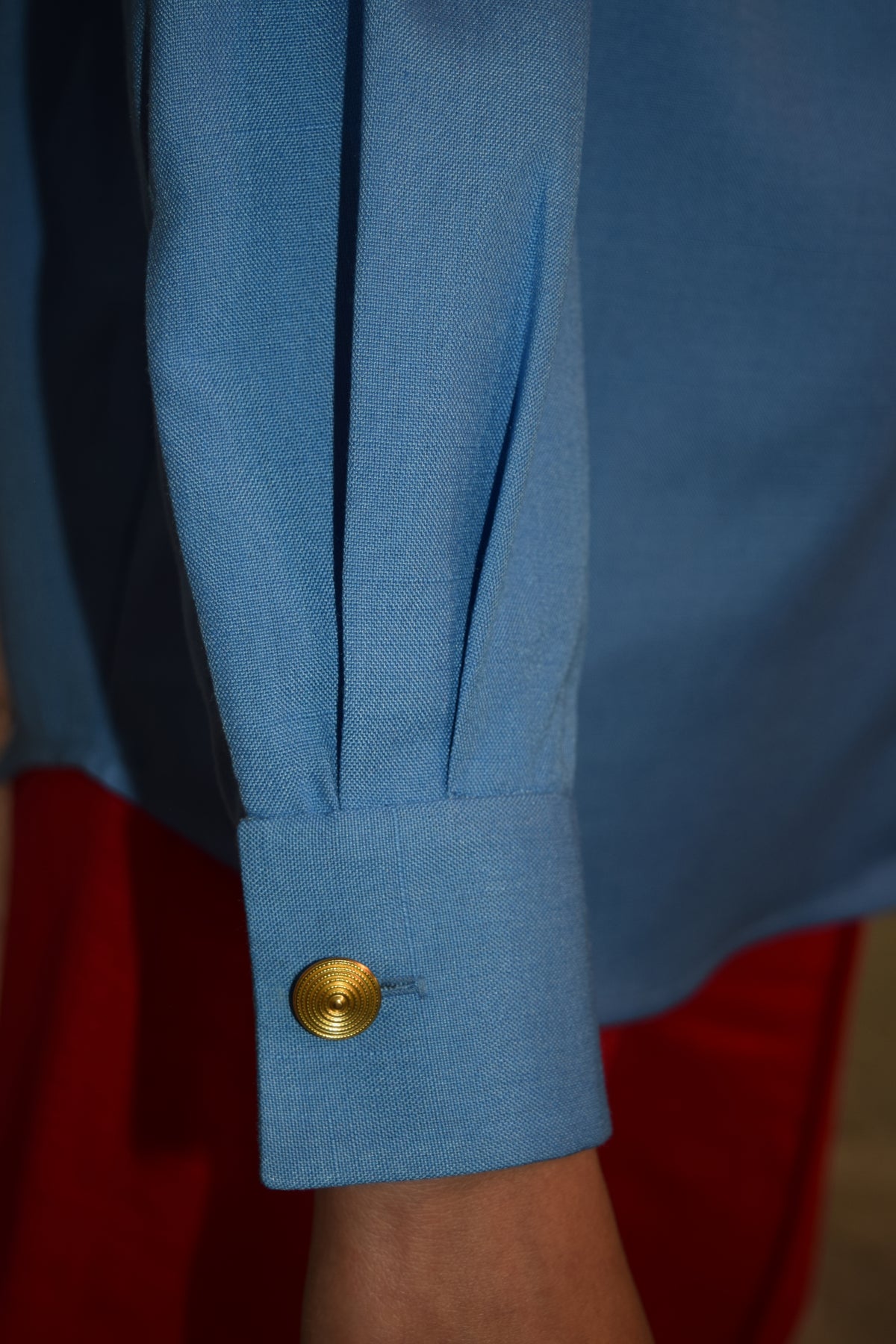 Close-up of a blue shirt cuff with a gold button, blurred background