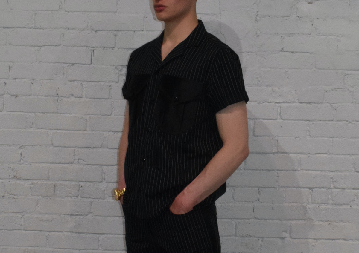 Person wearing a black pinstripe outfit against a white brick wall.