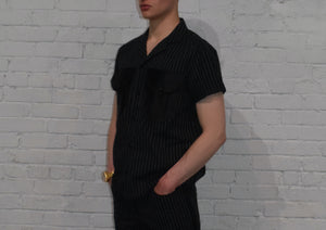 Person wearing a black pinstripe outfit against a white brick wall.
