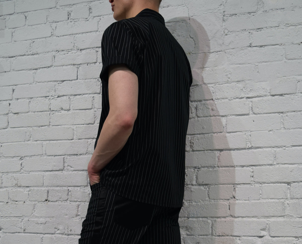 Person wearing a black outfit against a white brick wall