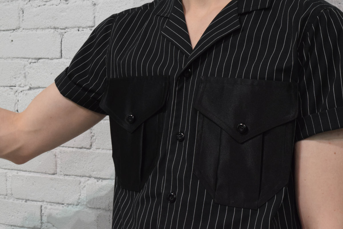 Person wearing a black pinstripe shirt against a white brick wall